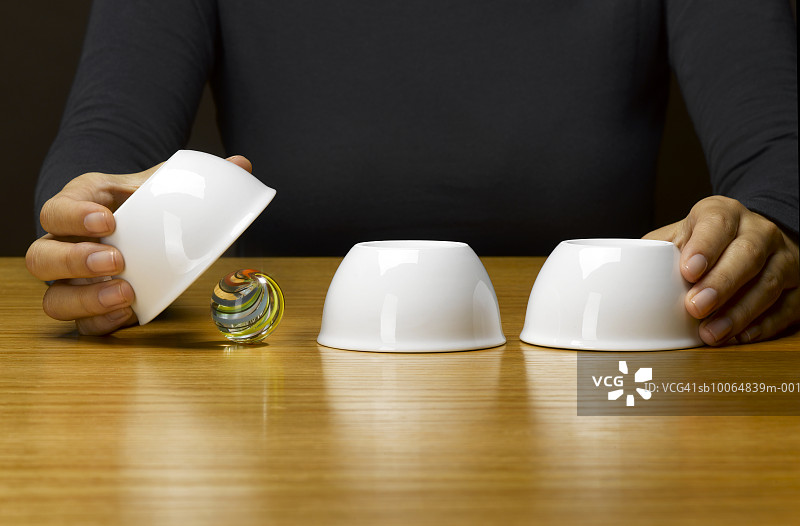 男人玩机会游戏，展示在翻倒的杯子下的弹珠，中间部分图片素材