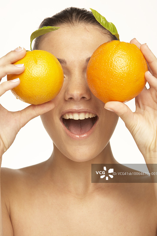 把橙子放在眼前，张开嘴的年轻女人图片素材