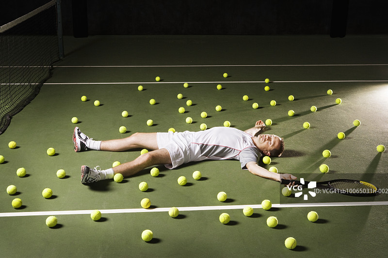 男人躺在网球场上，周围都是网球，高角度图片素材