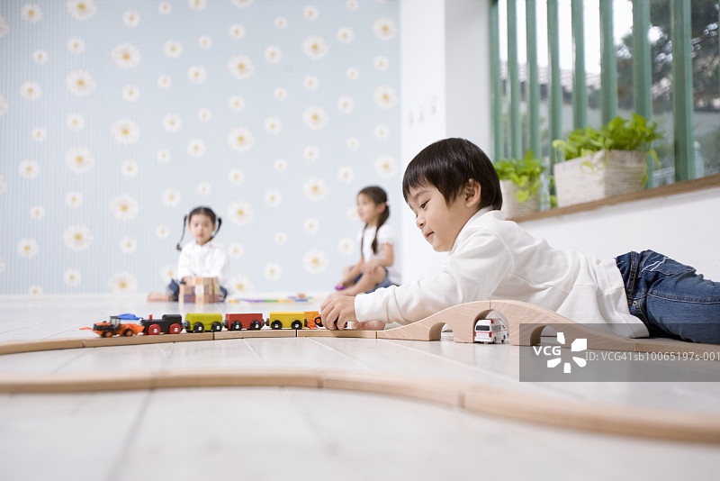 玩玩具火车的男孩，两个女孩坐在背景中图片素材