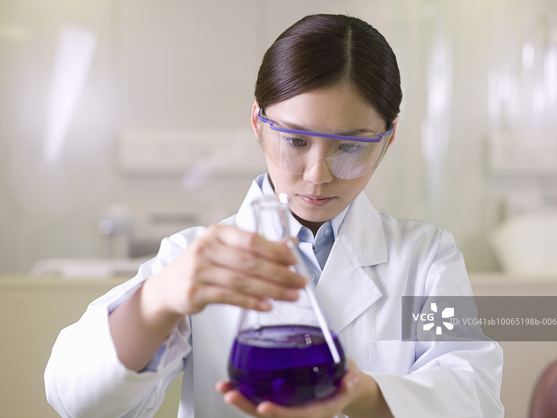 实验室里手持紫色液体的烧瓶的女人图片素材