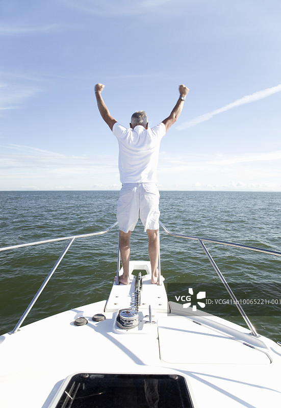 站在游艇船头，张开双臂的中年男人（后视图）图片素材
