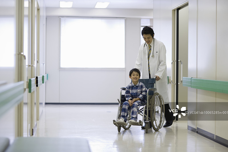 医生在医院走廊推着坐轮椅的男孩图片素材