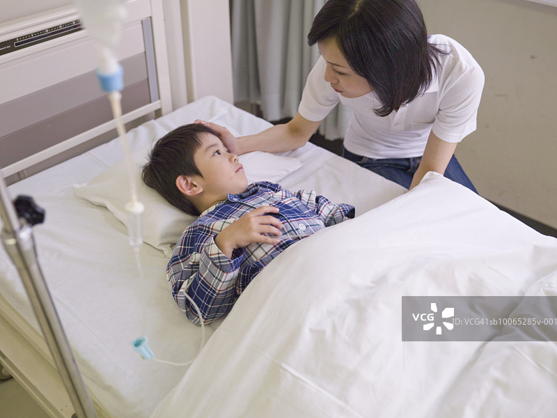 医院病床上，母亲陪伴着正在输液的男孩图片素材