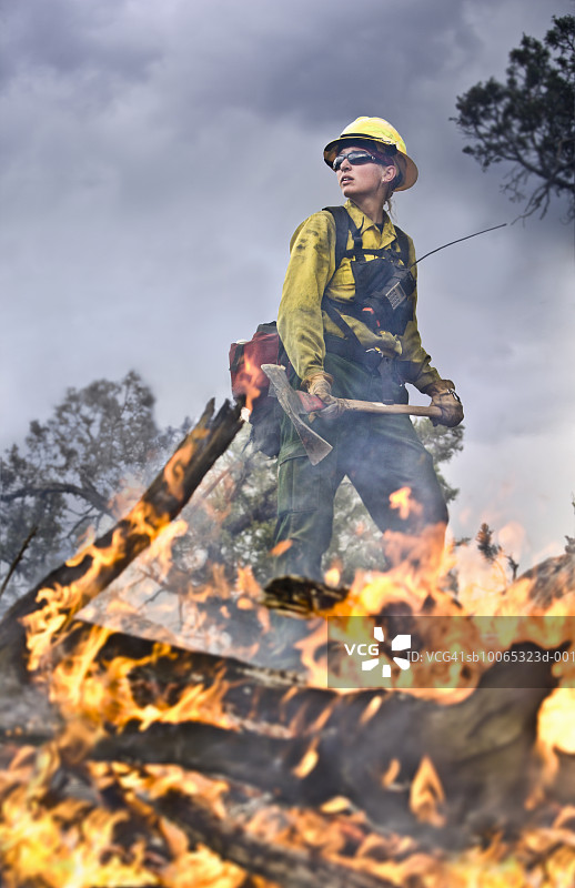 女消防员拿着镐在燃烧的树枝附近图片素材