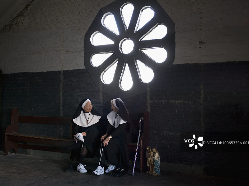 两位年长的修女坐在长凳上聊天并系鞋带图片素材