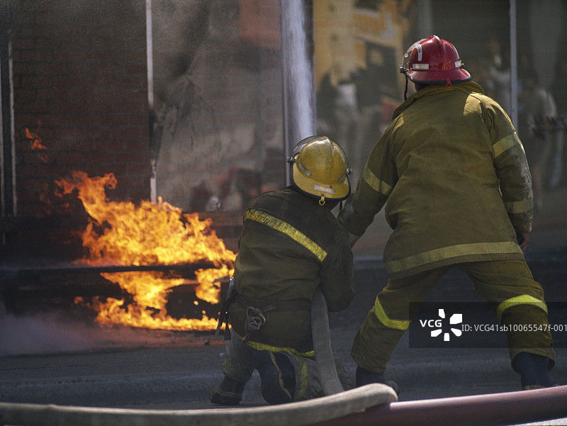 两名消防员喷洒燃烧的建筑物（后视图）图片素材