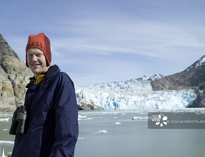 站在冰川旁微笑的男人肖像，手持双筒望远镜图片素材