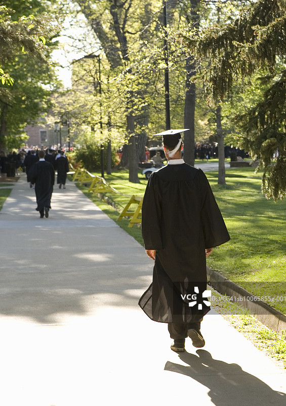 毕业生戴着学士帽和学士服在校园里行走，后视图图片素材