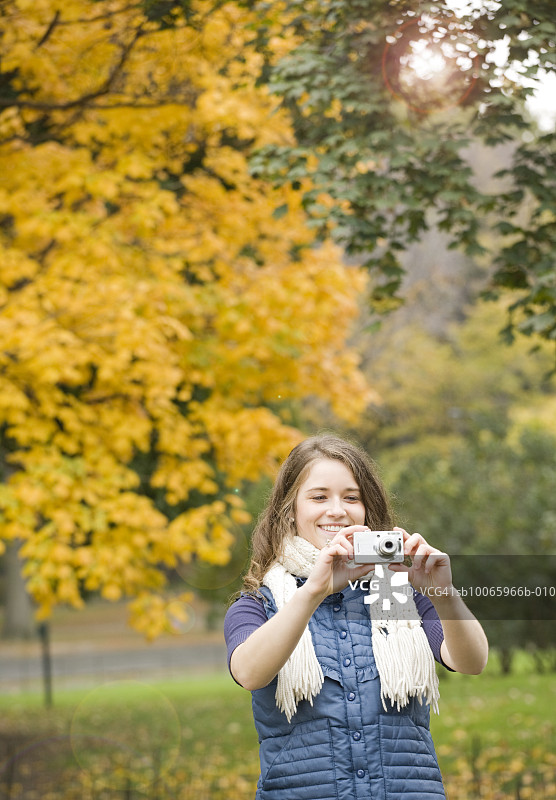 年轻女人在公园里用数码相机拍照，面带微笑图片素材