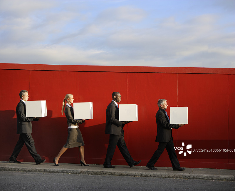 在红墙前拿着白色盒子行走的四个商人，侧视图图片素材