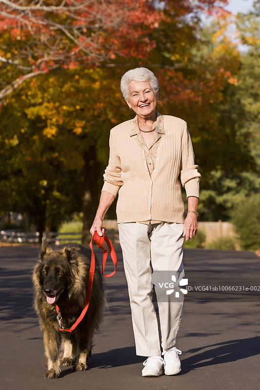 年长的女人带着德国牧羊犬在街上散步，面带微笑图片素材