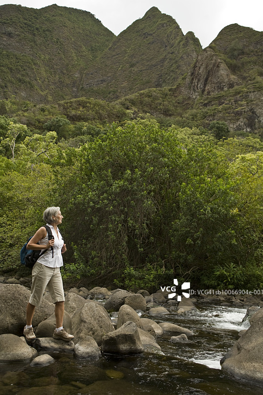 女人站在山间溪流旁的岩石上图片素材