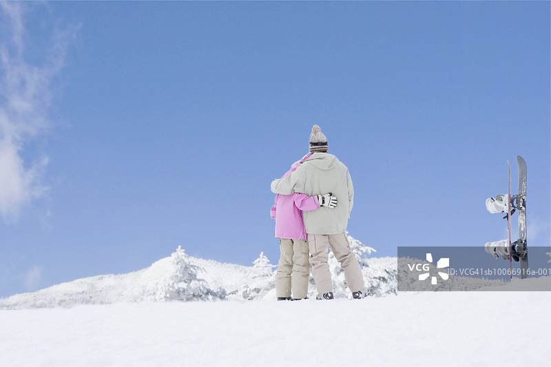 在雪山上的滑雪板旁拥抱的情侣图片素材