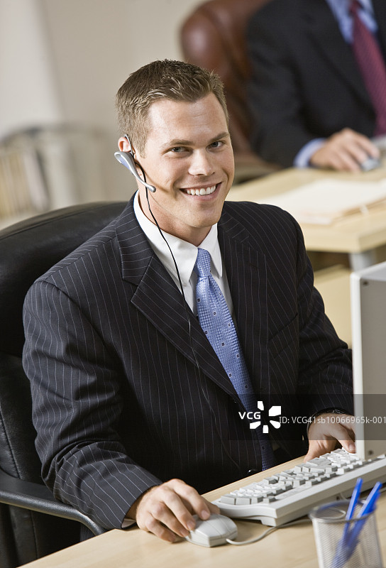 戴着电话耳机用电脑工作的年轻人图片素材