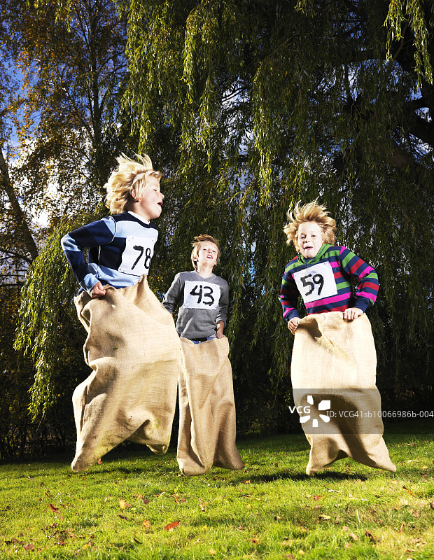 三个男孩（8-11岁）在公园里进行麻袋赛跑图片素材