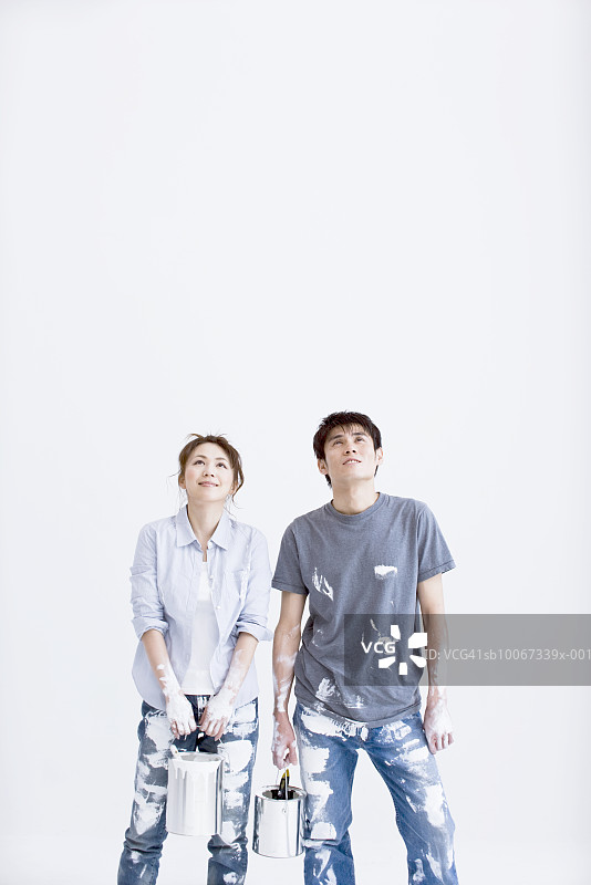 年轻夫妇在新家拿着油漆罐，身穿沾满油漆的衣服图片素材
