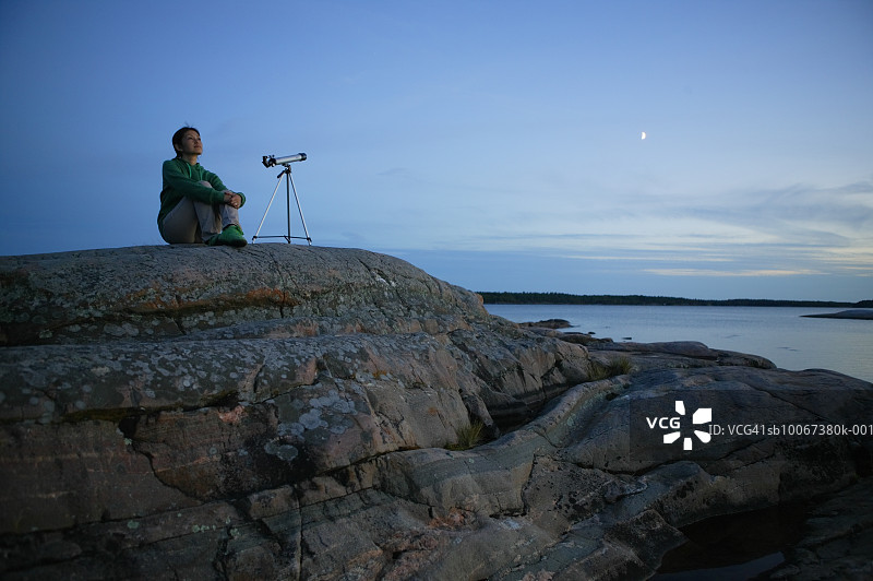 黄昏时坐在海边的用望远镜的女人图片素材