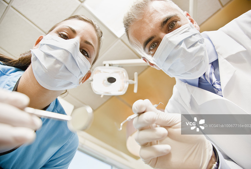 牙医和女牙科助手拿着牙科工具的特写肖像，低角度拍摄图片素材
