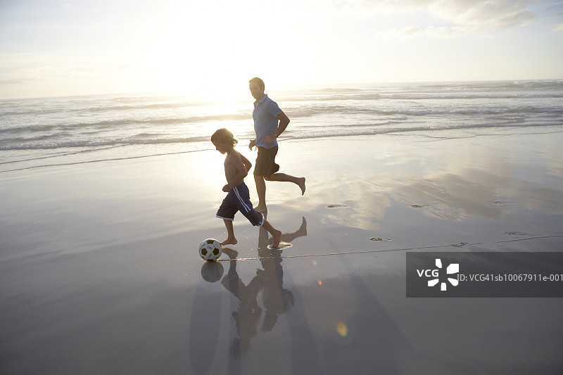 父亲和儿子（6-7岁）在海滩上玩足球，侧视图图片素材