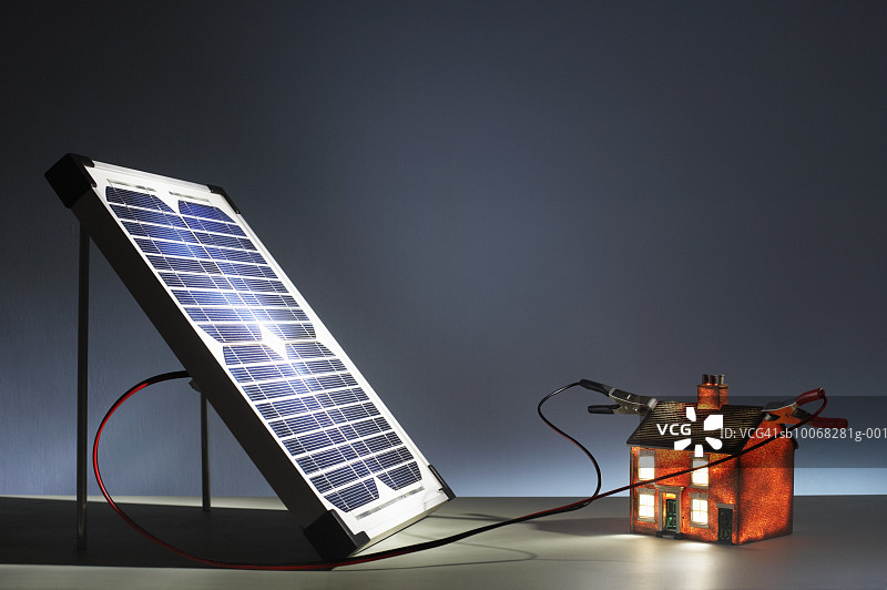 连接到发光模型房屋的太阳能电池板特写图片素材