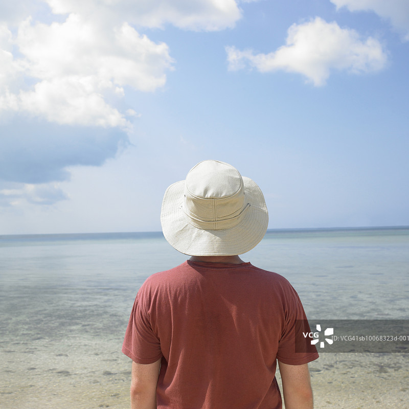 戴着帽子的年轻男人望着大海，后视图图片素材
