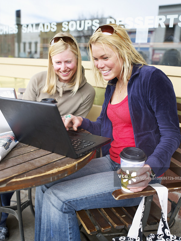 两名年轻女子在咖啡馆使用笔记本电脑微笑图片素材