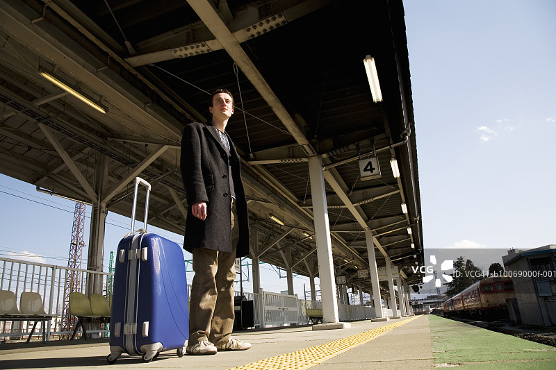 站在站台上拿着手提箱的年轻男子，低角度视图图片素材