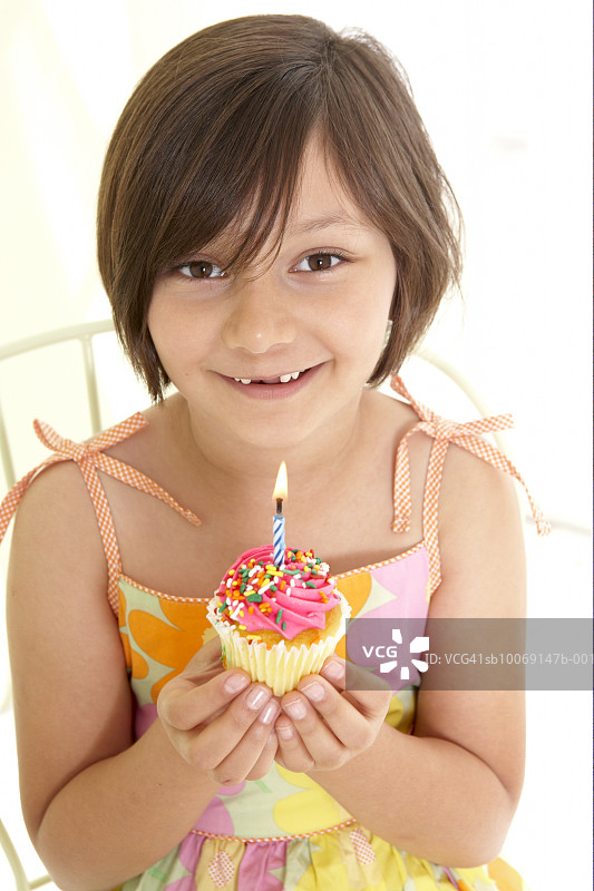 手持点燃蜡烛的纸杯蛋糕的女孩（6-7岁）的肖像图片素材