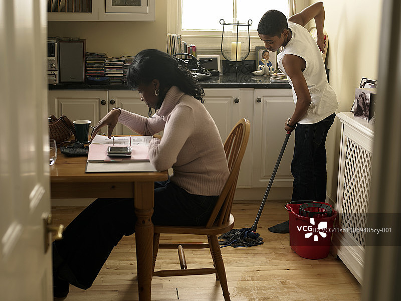 母亲在数钞票，男孩（12-13岁）在后面拖地图片素材