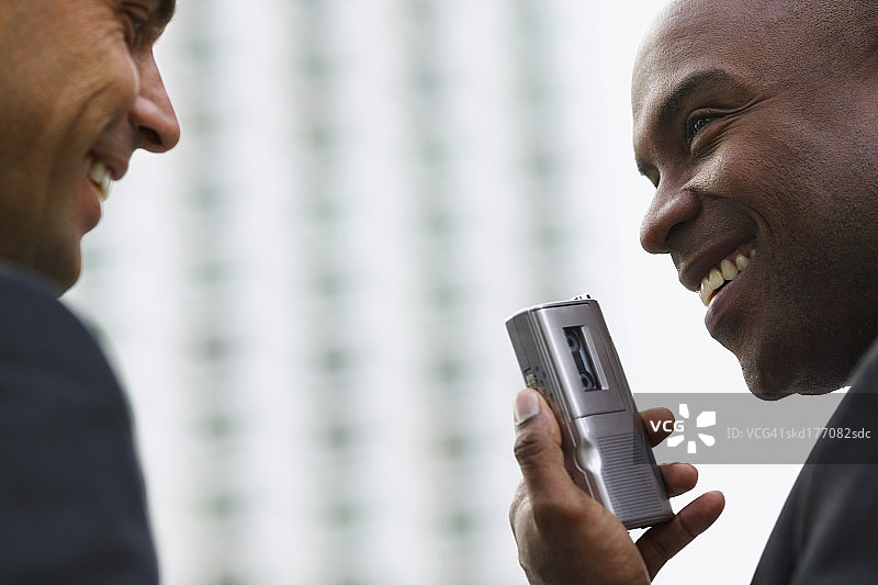 两位商人交谈，其中一位拿着录音机的特写图片素材