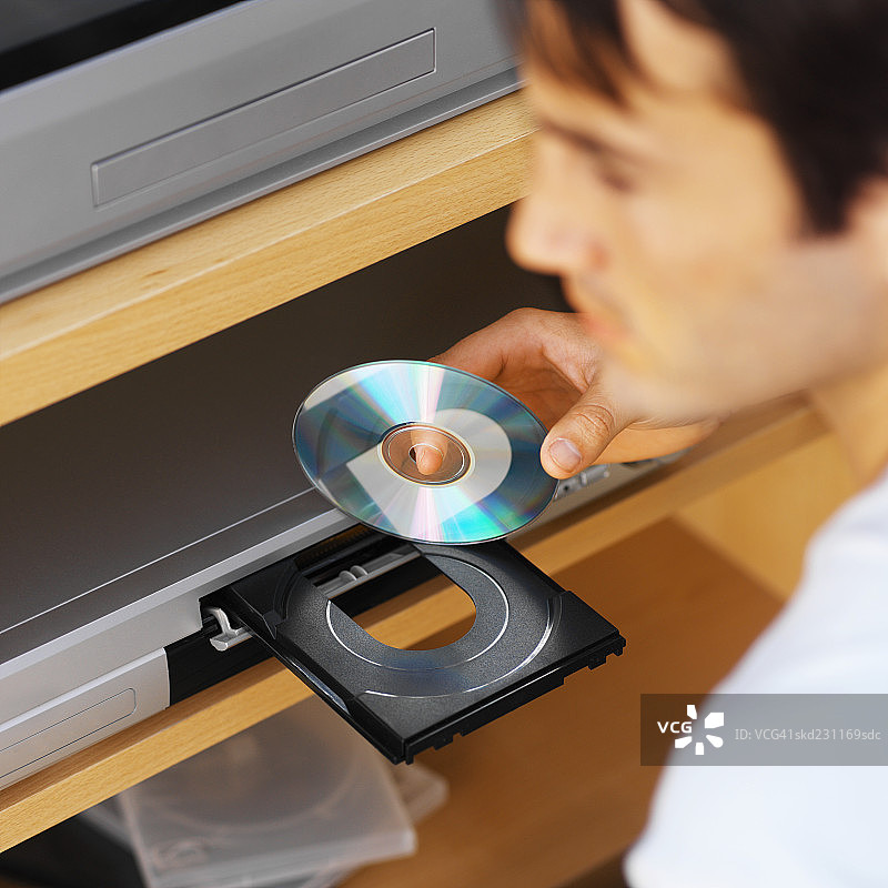年轻男人将DVD插入DVD播放机的高空特写镜头图片素材