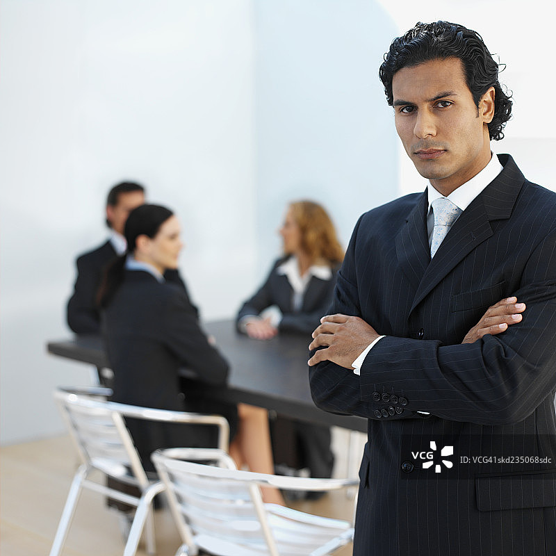 三位商务高管坐在会议室里，第四位高管站立，双臂交叉图片素材