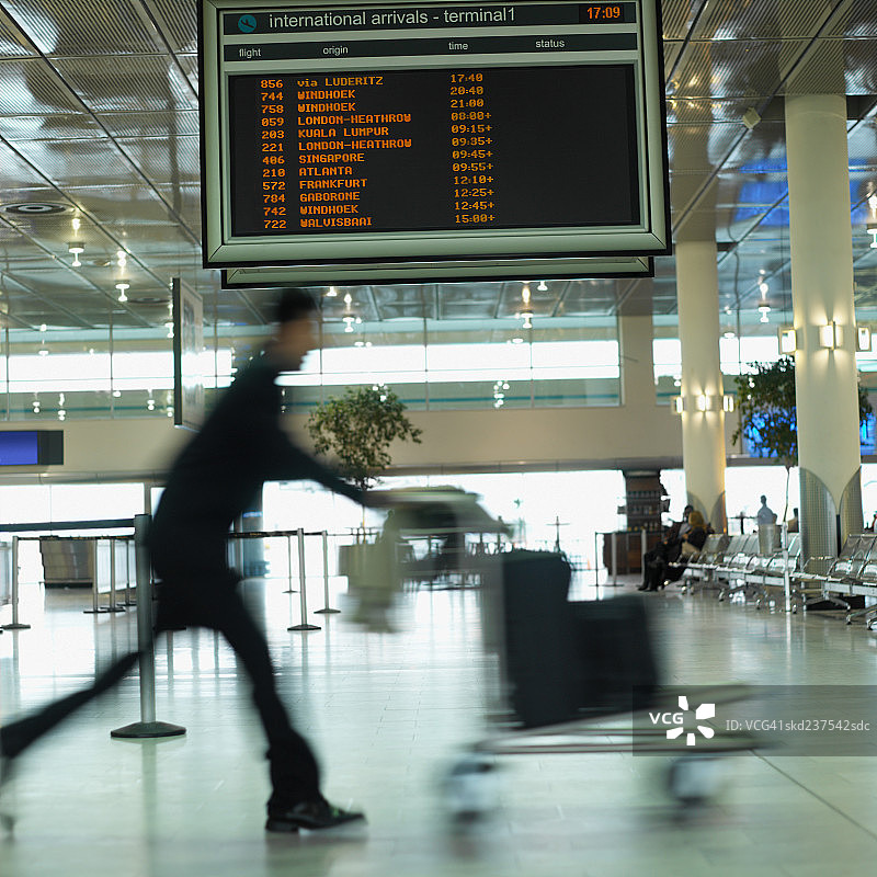 在机场行走并推着行李推车的男商人图片素材