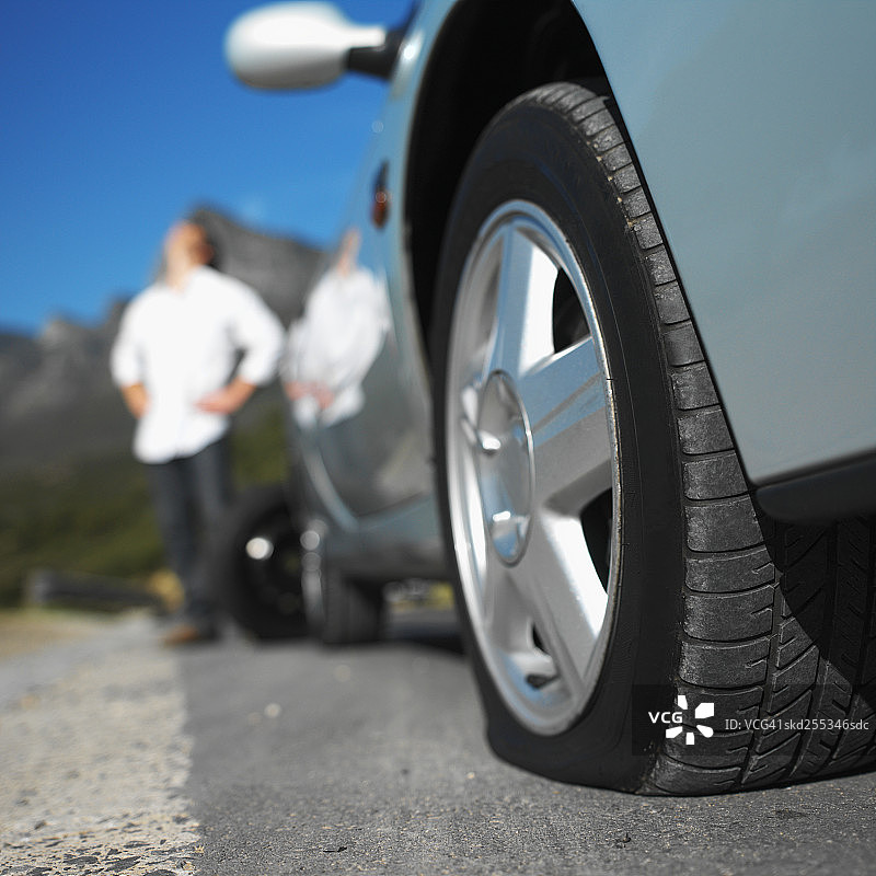 汽车轮胎漏气，年轻男子束手无策的特写镜头图片素材