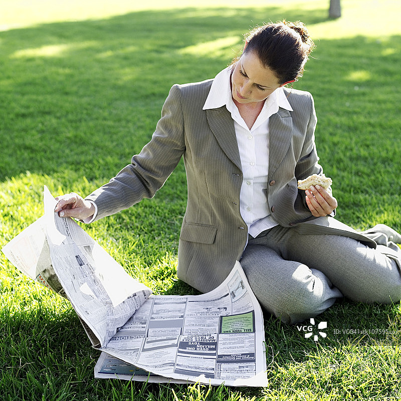 女商人坐在草坪上吃三明治，读报纸图片素材