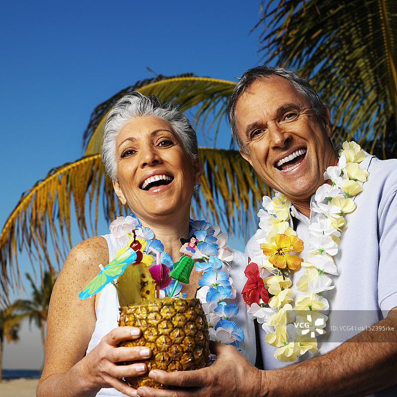 老年夫妇微笑地拿着菠萝果汁饮料，戴着花环的肖像图片素材