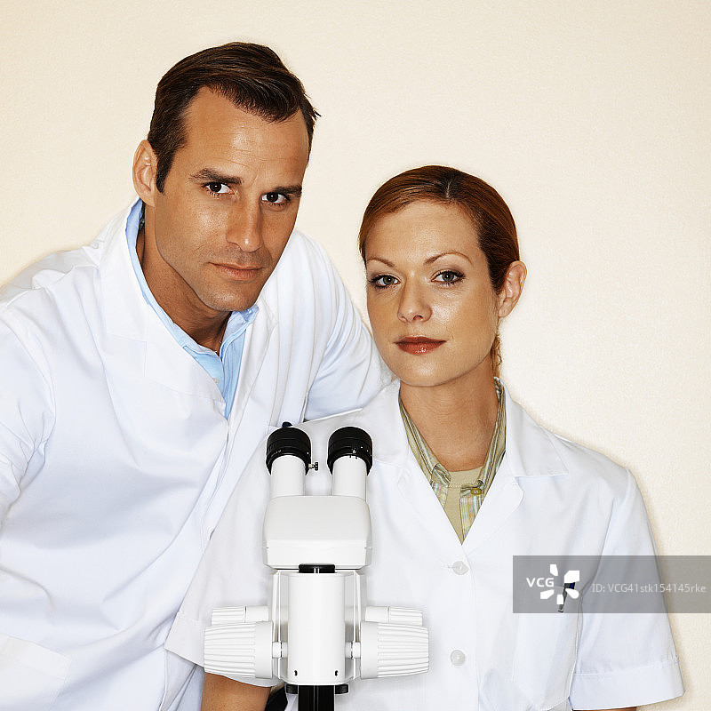 两位年轻微生物学家看着相机，显微镜在前的肖像图片素材