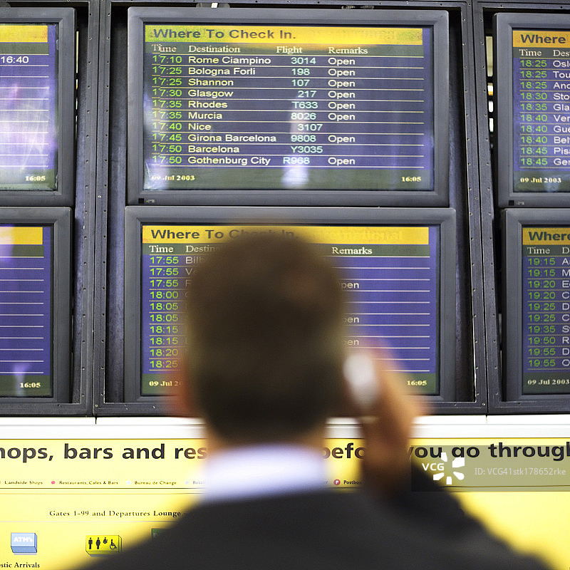 男人拿着手机站在航班时刻表前图片素材