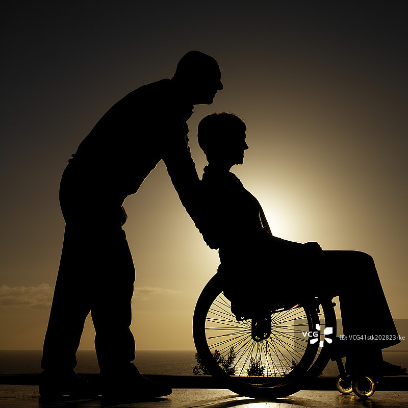 男子推着坐在轮椅上的女子的侧影图片素材