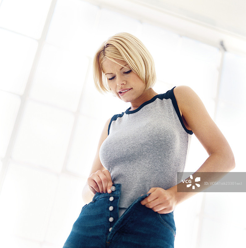 低角度拍摄：一位女士试图扣上牛仔裤图片素材