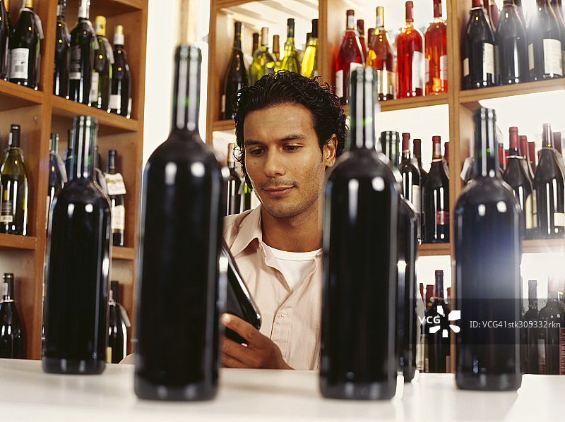 在酒类商店阅读葡萄酒标签的年轻男人图片素材
