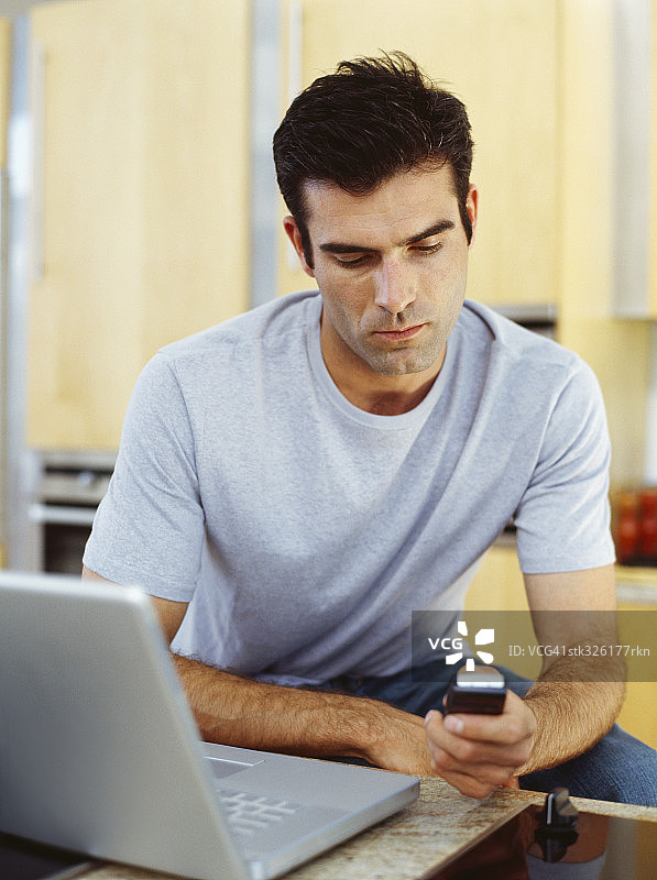 坐在笔记本电脑前使用手机的中年男人图片素材