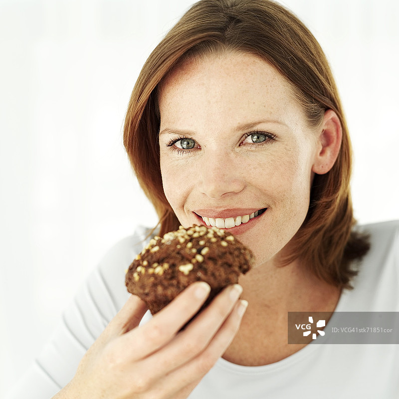 年轻女人手拿巧克力松饼放至嘴边肖像图片素材