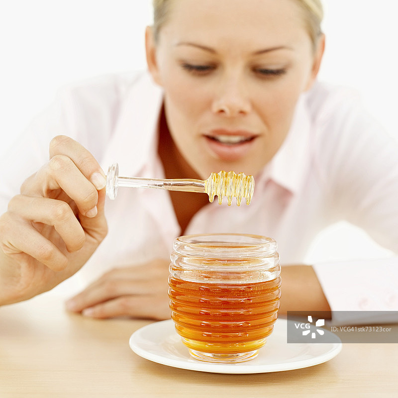 女人拿着蜂蜜勺子在蜂蜜罐上方特写图片素材