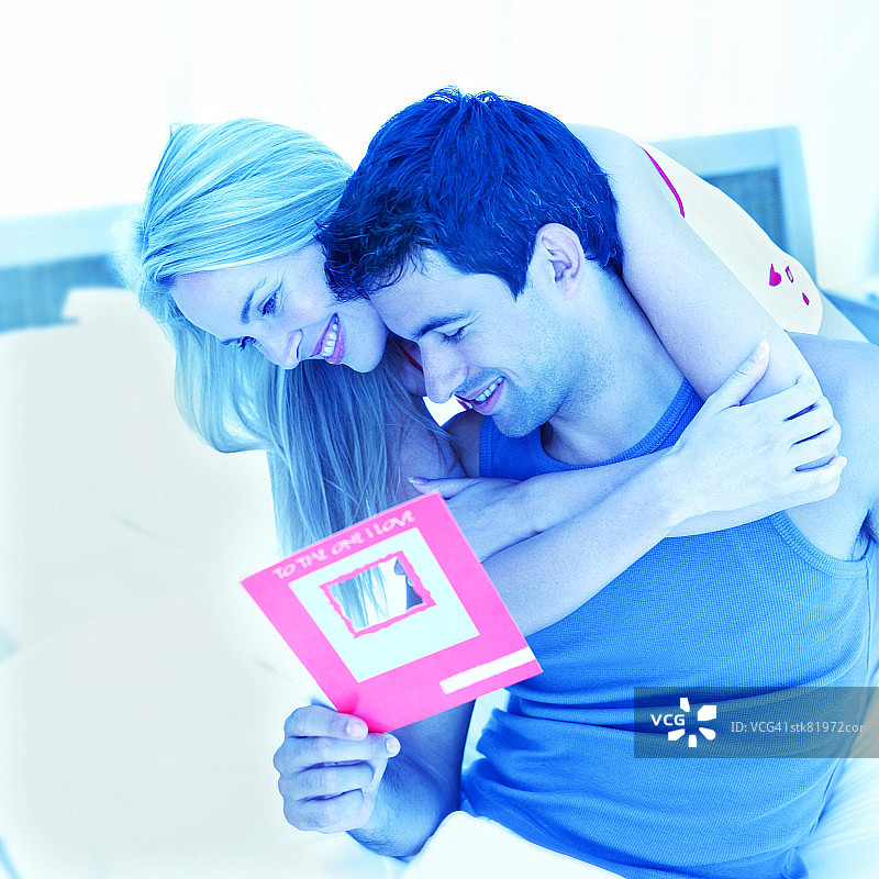 年轻夫妇在床上阅读卡片并拥抱的肖像图片素材