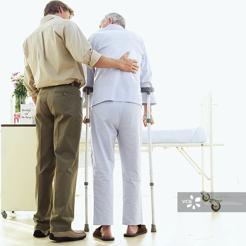 男子帮助老年人拄拐杖行走的背影图片素材