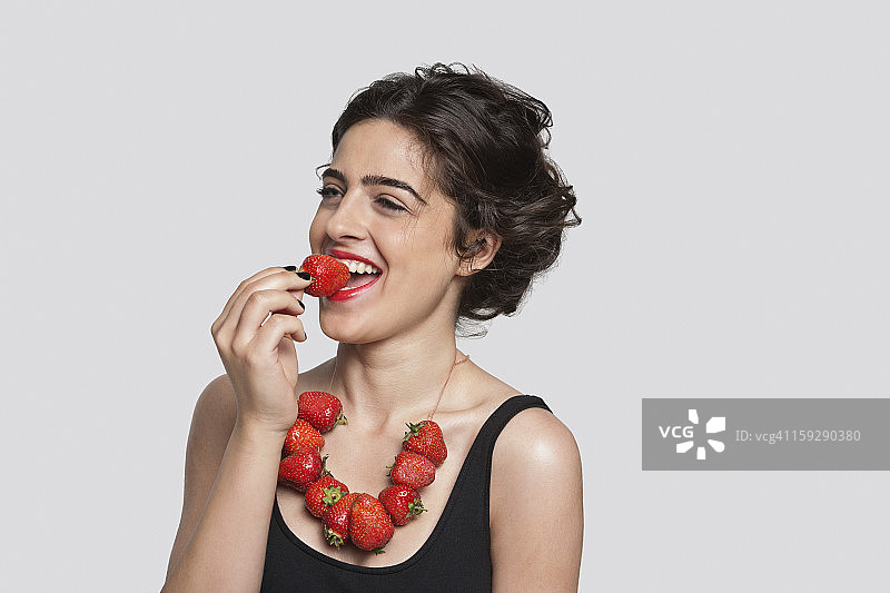 戴着草莓项链，吃草莓的快乐年轻女人图片素材