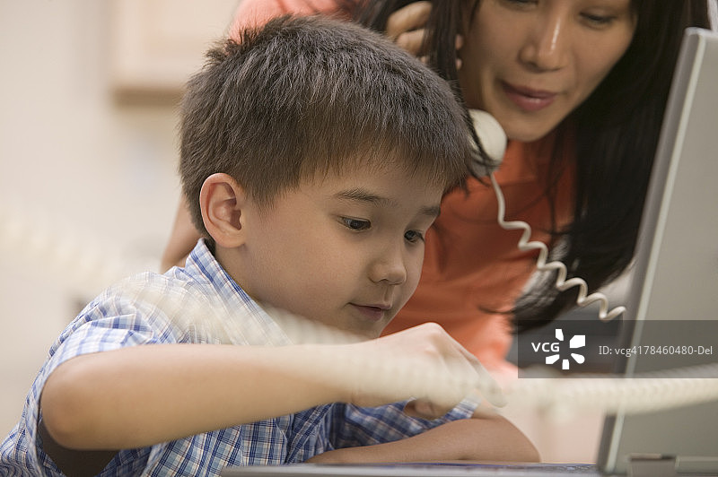 母亲在打电话，看着儿子使用笔记本电脑图片素材