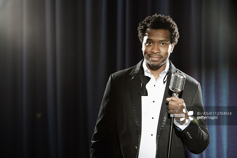 身穿燕尾服站在麦克风前的黑人男子，面带笑容图片素材